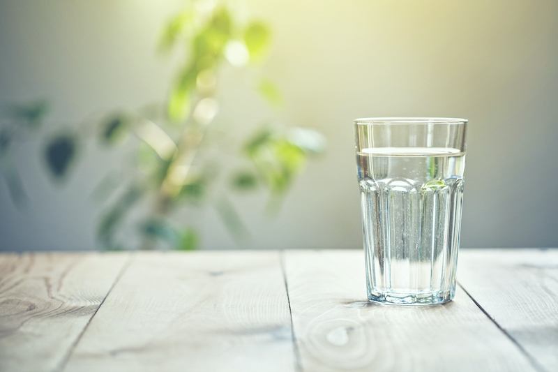 Glass of pure water on sunlight background with natural plant