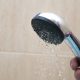 A hand holding a detachable shower head with slow water flow from hard water