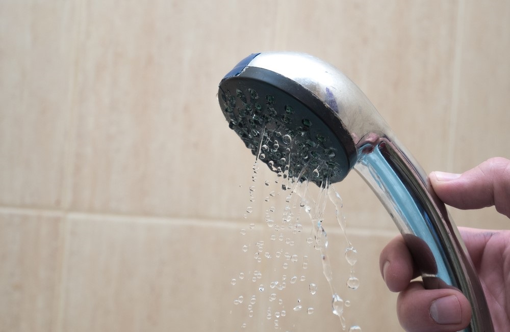 A hand holding a detachable shower head with slow water flow from hard water