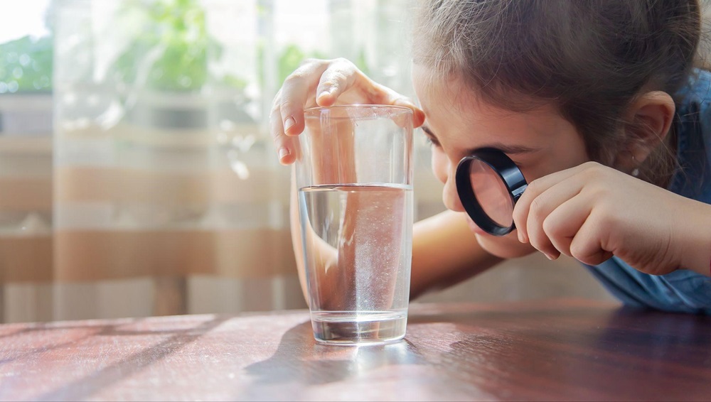 Young child examining a glass of water with a magnifying glass