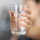 woman out of focus holding a glass of water to camera